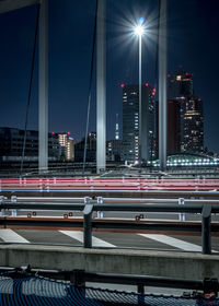 Light trails on road by buildings against sky at night