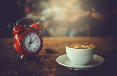 Close-up of coffee cup by alarm clock on table