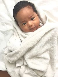 High angle portrait of cute baby boy wrapped in towel lying on bed at home