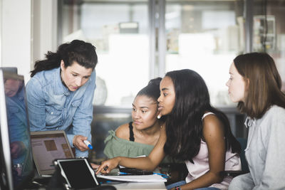 Mature teacher and female students discussing over laptop in computer lab at high school