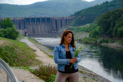 Portrait of young woman standing on bridge against mountains