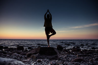 Full length of man exercising at beach against sky during sunset