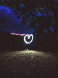 People doing light painting on field against sky at night