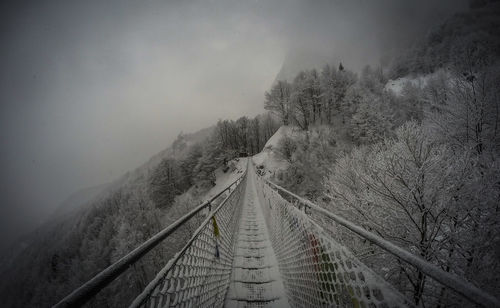 Footbridge over snow covered trees against sky