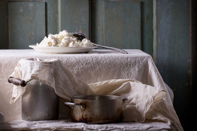 Plate of homemade cottage cheese served with vintage aluminum pan and water-can on white tablecloth with turquoise wooden background