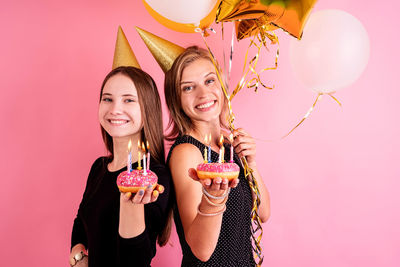 Portrait of a smiling young woman holding pink balloons against colored background