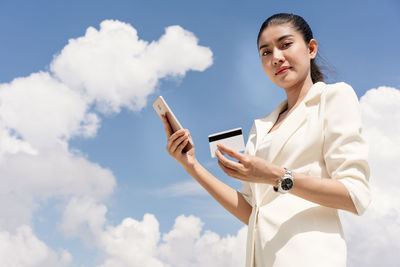 Low angle view of woman using smart phone against sky