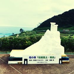 Close-up of information sign on beach against sky