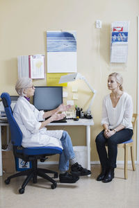 Full length of senior female doctor talking with woman in clinic