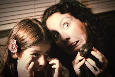 Playful mother and daughter making faces while holding kitten