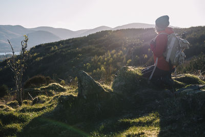 Woman kneeling on grass against mountains