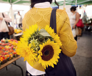 Rear view of woman carrying sunflowers in purse at market