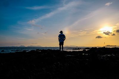 Rear view of man standing on shore during sunset