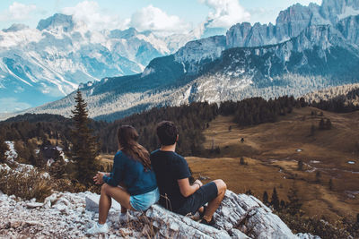 Rear view of friends sitting on rock against mountains