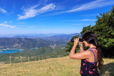 Woman looking through binoculars while standing on land