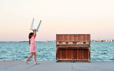 Little girl carries piano stool for outdoor playing at the sea