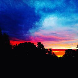 Silhouette trees against dramatic sky during sunset