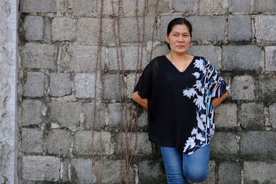 Portrait of smiling woman standing against brick wall