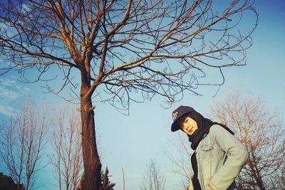 Side view of man standing by bare trees against sky