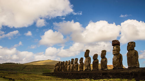 Ancient statues on field against sky