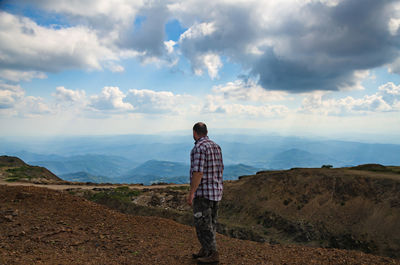 Rear view of man standing on mountain against sky