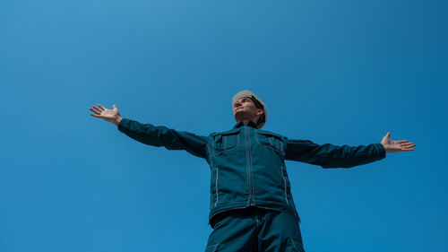 Full length of woman with arms raised standing against clear blue sky