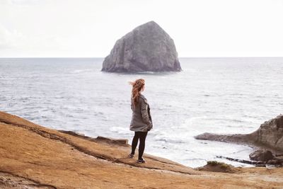 Rear view of woman standing on rock by sea against clear sky