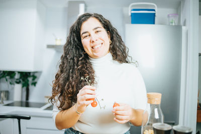 Portrait of smiling woman holding food in kitchen