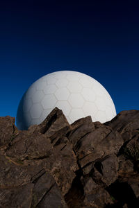 Low angle view of communication towers by rocks against clear blue sky