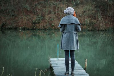 Rear view of woman standing on pier over lake