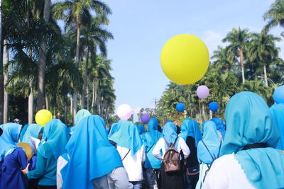 Rear view of women with helium balloons against clear sky