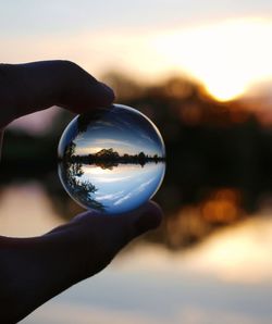 Close-up of hand holding glass of crystal ball against sunset sky