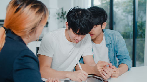 Agent by gay men signing over digital tablet on table