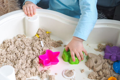 Faceless baby boy is playing with kinetic sand and colorful molds on the table