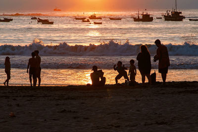 Silhouette people on beach against sky during sunset