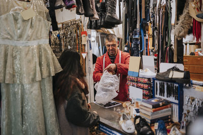 Rear view of female customer talking with store owner holding plastic bag