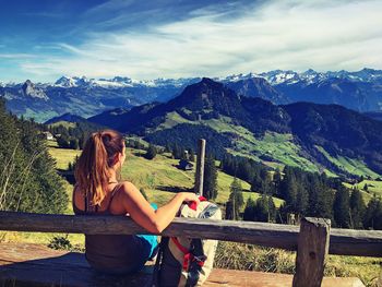 Woman sitting on bench over mountains against sky