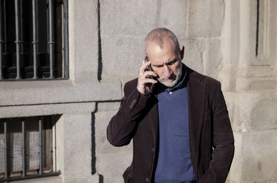 Adult man in suit talking on mobile phone against white stone wall