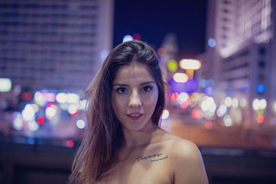 Portrait of young woman at illuminated city