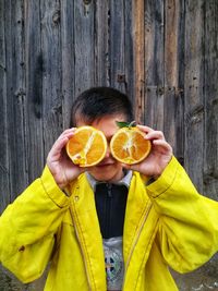 Boy holding orange while standing against wooden fence