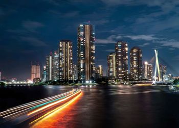 Light trails on illuminated buildings against sky at night