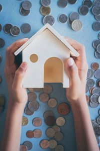 Cropped image of hands holding model house over coins