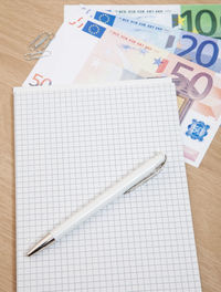 High angle view of pen and note pad with various euro notes on table