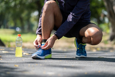 Low section of man tying shoelace by bottle on road