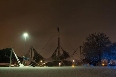 Illuminated street lights by trees against sky at night