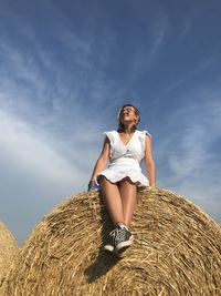 Low angle view of smiling teenage girl wearing sunglasses while sitting on hay bale 