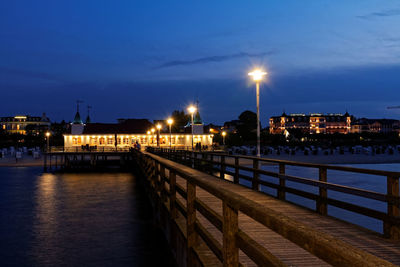 Illuminated street by river against sky at night