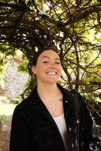 Portrait of young woman standing against tree