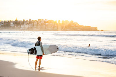Rear view of man with surfboard at beach against sky