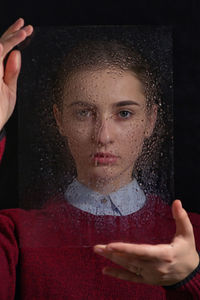 Portrait of woman holding wet glass against black background